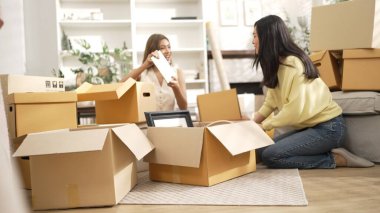 İki kız yeni eve taşınıyor ve oturuyorlar ve kutuları açıyorlar. Ev arkadaşı karton kutuyla çevrili oturma odasında konuşurken dekorasyonu kutudan çıkarıyor. Yeniden yerleştirme. Myrmidon.