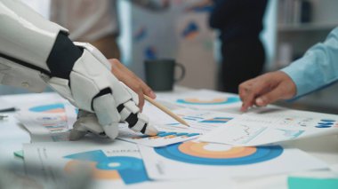 Robotik el, modern iş uygulamalarında teknolojinin entegrasyonunu vurgulayarak, çeşitli grafik ve grafikleri analiz etmede insanlarla işbirliği içindedir.