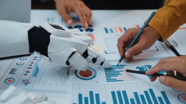 Bir insan eli ve robot el, grafikler ve çizelgeler ile çevrili veri analizi üzerinde birlikte çalışırlar. Bu sahne takım çalışmasının geleceğini dijital ortamda somutlaştırıyor. Noogenesis