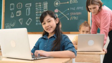 Akıllı Asyalı kız, mühendislik komut yazarken kameraya bakıyor. Çok kültürlü bir öğrenci yapay zekayı öğrenirken öğretmenler sistemi öğretiyor ya da STEM sınıfında sınıfları kontrol ediyor. Pedagoji.