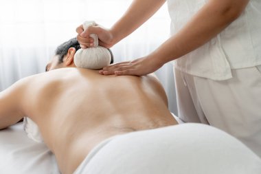 Sıcak bitkisel top spa masaj vücut tedavisi, masör erkek vücuduna nazikçe şifalı bitki torbası bastırıyor. Aromaterapi dinlenme sükuneti ve sükuneti kaplıca salonundaki atmosferi aydınlatıyor. Sessiz.