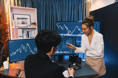 PC ekranlarında dinamik borsa istatistiklerini tartışan iş ortaklarının kağıt üzerinde not alması, para birimi grafiğindeki yüksek ya da düşük nokta ile gece neon çağındaki modern ofis karşılaştırıldığında. İnfobahn.