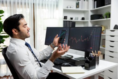 Akıllı telefondan akıllı telefon arayan tüccar işadamı, bilgisayardaki dinamik borsa yatırım ekranını analiz ediyor ve modern merkez ofisteki en kârlı finansal teknoloji pazarına yatırım yapıyor. Tahmin et..