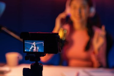 Güzel Asyalı bir kanalın sunucusundaki seçici odak kamera ekranı dinleyiciyle sosyal medyada müzik dinliyor, bulanık arka planda mikrofon kullanarak pastel kulaklık takıyor. Taktik.