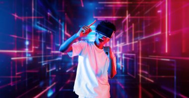 VR gözlüklü profesyonel erkek oyuncu parlayan neon ışıkla oyun oynuyor. Heyecanlı oyuncu artırılmış gerçeklik teknolojisi yeniliklerini kullanarak metaevrene bağlanmayı seviyor. Yaratıcılık.