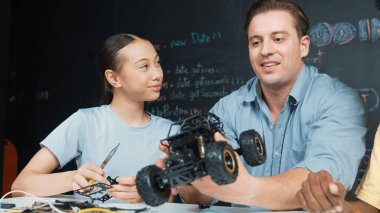 Akıllı öğretmen araba modelini farklı öğrencilere denetliyor. Karışık ırk dinleyicisi olan liseli çocuklar masadaki dizüstü bilgisayarlı ve kablolu robot model sistemini açıklıyor. Öğretim.