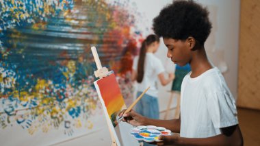 Afrikalı erkek tuvali sıcak tonda boyarken, beyaz elbiseli kız renkli duvarın arkasında havalı renkler çiziyor. Yaratıcı aktivite konsepti. Öğretim.