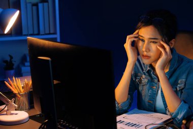 Stresli, genç, güzel Asyalı yaratıcı proje yaratıcısı sosyal medyayı araştırmak için bilgisayara bakıyor ve geceleri daha çok neon modern ofisin planlama kanalı stratejisine ulaşılıyor. Taktik.