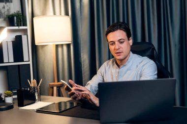 Akıllı iş adamı, müşterilerle veya yatırımcılarla iletişim kurmak için akıllı telefonuyla çalışır. Laptop ve tablet veritabanında geceleri mavi perde arkasında iş hedefiyle birlikte araştırma yapar. Bireysel.