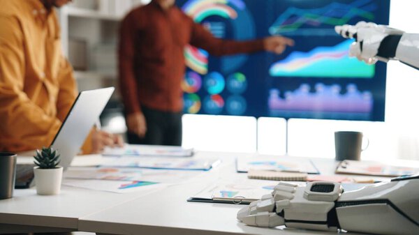 In a contemporary office setting, professionals engage in a meeting with a robotic element, analyzing data and discussing strategies through vibrant charts and graphs.Noogenesis
