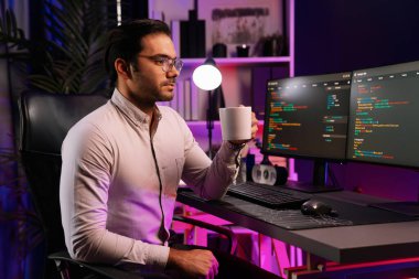 Akıllı IT geliştiricisi, bilgisayar ekranında yazılım geliştirme kodlu kahve fincanı tutuyor. Dışarıya bakıyor, program güncellemesi internet sitesi verilerini neon ışıklı siber ofiste sunuyor. Tahmin et..