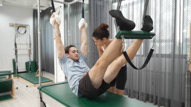 Eğitmen rehberliğinde Pilates Cadillac 'ta ters bacak yükseltme pratiği yapan sağlıklı bir müşteri. Çekirdek dayanıklılığını ve üst vücut dengesini arttırmak için Cadillac 'ı geren adam. Alışkanlık.