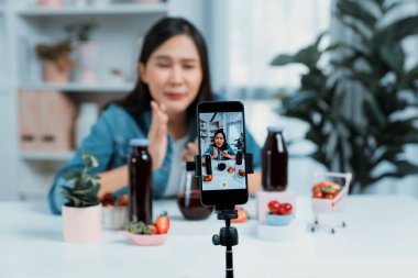 Seçici odaklı akıllı telefon ve gülümseyen genç, güzel Asyalı karışık çilek ve kiraz suyu detoksu değerlendirmesi sosyal medyada sağlıklı ürün tanıtımı sunuyor. Taktik.