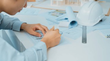 Profesyonel mimar taslak çiziyor ve güvenlik kaskı, ev modeli ve planlarla toplantı masasında genç ve güzel beyaz iş arkadaşıyla birlikte çalışıyor. Tertemiz..