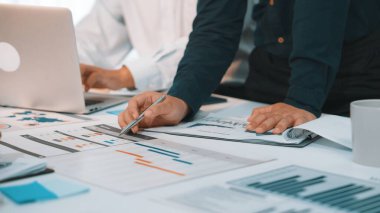 İş adamları, modern bir ofis alanında işbirliği yaparken finansal raporlar ve grafiklerin dinamik bir analizine giriştiler. Bir dizüstü bilgisayar ve evraklar çalışma alanını genişletir. SACTR