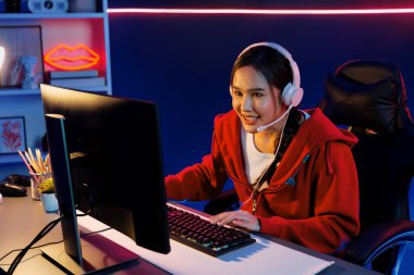 İnternet üzerinden kulaklık takıp gülümseyen Asyalı güzel kız flamasının sunucu kanalı izleyicilerle internet üzerinden konuşma yapıyor. Esport yetenekli takım oyuncuları neon mavi odada. Taktik.