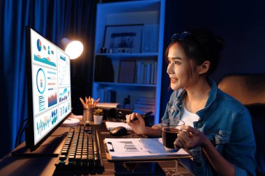 Elinde kahve fincanıyla bilgisayara bakan Asyalı güzel yaratıcı bir kadının iş piyasası grafik klasörü raporuna gece vakti işaret ettiğini düşünmek. Taktik.