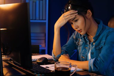 Stresli, genç, güzel Asyalı yaratıcı proje yaratıcısı sosyal medyayı araştırmak için bilgisayara bakıyor ve geceleri daha çok neon modern ofisin planlama kanalı stratejisine ulaşılıyor. Taktik.