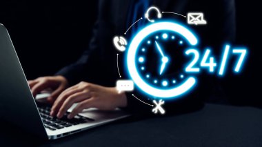 Bir iş adamı, kendisini çevreleyen simgelerle bir dizüstü bilgisayara yazı yazarak, modern dijital çalışma ortamında 24 saatlik iletişim ve destek olanağını sembolize ediyor. Dörtgen