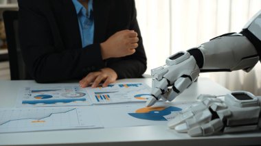 Bir insan ve robot eli gösteren büyüleyici bir sahne bir iş toplantısında verileri tabloda gösterilen tablolar ve raporlarla analiz ediyor. Noogenesis