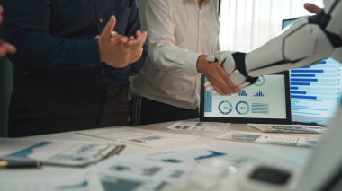 Modern bir ofiste işbirliği yapan bir insan ve robotun sergilendiği dinamik bir iş toplantısı. Sahnede ekip çalışması, teknoloji ve büyüme için yenilikçi çözümler vurgulanıyor. Noogenesis