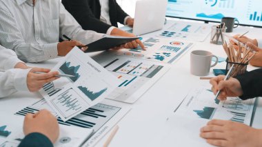 Çeşitli bir iş ekibi, kağıt ve dijital cihazlarda gösterilen grafikler ve grafikler üzerine ayrıntılı bir tartışmaya girişerek, işbirliğini ve strateji gelişimini teşvik ediyor. SACTR