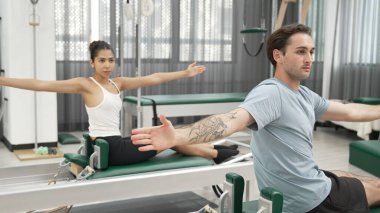 Pilates reformatör makinelerinde senkronize kol uzantıları yapan iki müşteri. Mutlu pilates partnerleri, esnekliği arttırmak ve dengeyi ve kontrolü sağlamak için reformcunun üzerine oturdular. Alışkanlık.