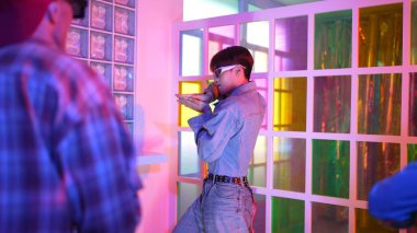 Ortasında dans eden profesyonel mutlu hipster onu alkışlayan çeşitli arkadaşlarıyla dans ediyor. Çekici Asyalı kırığı gece kulübünde neon ışığıyla enerjik adımlar atıyor. Mutluluk.