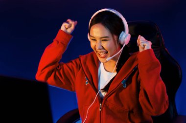 Yüzünde kulaklık renginde kulaklık takan, neon odada online oyun oynayan, Esport meziyetli takım oyuncularına yumruk kaldırarak oynayan güzel Asyalı kız flamasının sunucu kanalı. Taktik.