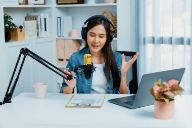 Sosyal medyada kulaklıkla canlı yayın yapan Asyalı sunucu modern stüdyoda yaşam koçluğu veya pazarlama dinleyicilerini selamlıyor. Taktik.