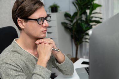 Modern ofiste oturan akıllı bir ofis çalışanı, ciddi bir yüz ifadesi olan, güzel görünümlü gözlük takan bir kamera. Yeni bir profil üzerinde sıradan bir günde çalışan iş adamı kavramı. Bireysel.