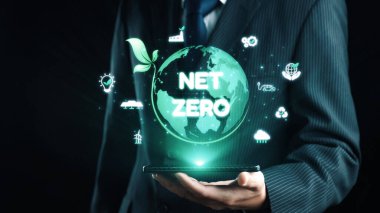 Bir işadamı, sürdürülebilirlik ve çevresel sorumluluğun önemini sembolize eden yeşil bir küre ve net sıfır konseptin dijital görüntüsünü akıllı telefona sunuyor. Dörtgen