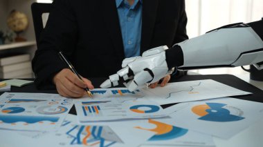 Bir insan ve robotik el, bir iş toplantısı sırasında veri analizine girişerek, grafikler ve grafikler yoluyla modern işyerlerinde teknolojinin entegrasyonunu gösteriyor.