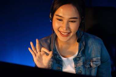 Sunucu kanalı Asyalı etkileyicisi canlı yayında konuşuyor. Sosyal medyada kulaklık takıyor, bilgisayar kaydı yapıyor, dinleyicileri selamlıyor ve Neon Modern Stüdyoları 'nda online olarak koçluk yapıyor. Taktik.