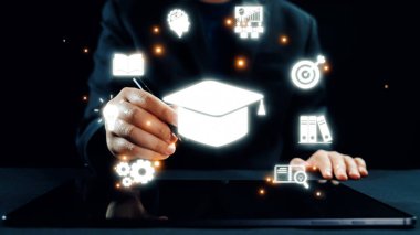 Bir kişi, dijital ortamda parlak eğitim simgelerini gösteren, bilgiyi, yeniliği ve modern öğrenme yöntemlerini sembolize eden bir tabletle etkileşime girer. Dörtgen