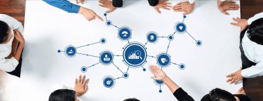 Çeşitli bir ekip, stratejik iş kavramlarını ve görsel veri sunumunu analiz ederek, etkin takım çalışması ve planlama becerilerini sergileyerek masa etrafında işbirliği yapar. Dostluk