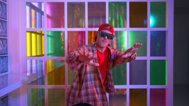 Komik break dansçı kameraya bakarken hiphop 'a doğru serbest adım atıyor. Çılgın mutlu hipster dans edip sokak dansı yaparken Led ışığında günlük kıyafet ve güneş gözlüğü takıyor. Mutluluk.