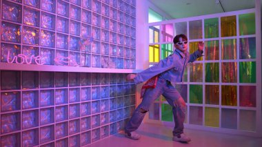 Gece kulübünde kameraya bakarken güneş gözlüklü Asyalı dansçı serbest dans ediyor. Mutlu sokak dansçısı dans ediyor ve renkli parlak neon ışığı ya da yol gösteren ışıkla ayak seslerini gösteriyor. Mutluluk.