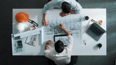 İnşaat mühendisinin bina tasarımını planlamak için birlikte çalıştığına dair üst düzey bir görüş. Yönetici planlar hakkında konuşurken ve tartışırken yetenekli mimar takımının yukarıdan görünüşü. Hizalama.