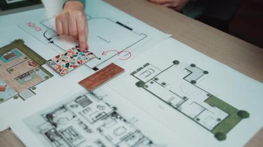 Modern bir çalışma alanı, renkli örnekler içeren mimari tasarım planları ve proje planlamasında yaratıcılığı ve organizasyonu yansıtan kalem tutan bir el sergiliyor. SACTR