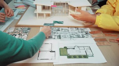 Merkezi bir masa üzerinde modern mimari, sergilenen planlar, materyaller ve çizimler üzerine odaklanmış bir ortak tasarım oturumunun yer aldığı canlı bir çalışma alanı. SACTR