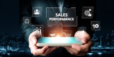 Profesyonel bir birey, dijital pazarlamanın modern iş dünyasına entegrasyonunu sembolize eden analitik simgelerle satış performans ölçümlerini gösteren bir akıllı telefon tutuyor. XDMCP