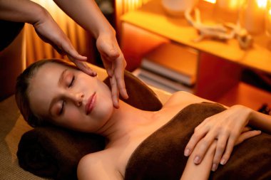 Beyaz kadın stres önleyici kafa masajı yapmaktan ve lüks otel veya otelde sıcak mum ışığında yüz güzelliği eğlencesi yapmaktan zevk alıyor. Sessiz.