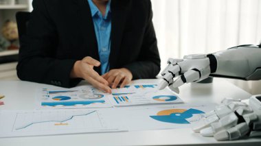 Bir insan ve bir robot, modern ofis ortamındaki teknolojik gelişmeleri vurgulayan çizelge ve grafikleri inceleyerek iş veri analizi üzerinde işbirliği yapıyor.