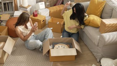 Lezbiyen aşıklar taşınma gününde karton kutudan nesneleri alıyorlar. Taşınırken paketleri açmak ve kutudan mobilya toplamak için birlikte çalışan bir çift oda arkadaşı. Yer değiştirme konsepti. Myrmidon.