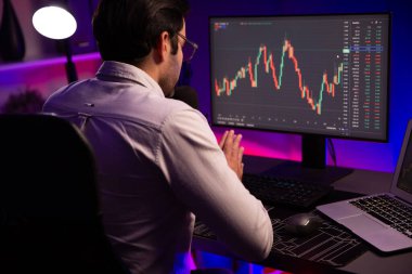 Akıllı tüccar işadamı, karanlık oda gecesinde neon ışıklı ofisteki arama pazarında yüksek kârla ekranda bilgisayar ve bilgisayar üzerinde dinamik borsa yatırımları üzerinde yoğunlaşıyor. Tahmin et..