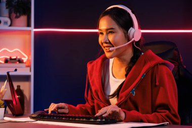 İnternet üzerinden kulaklık takıp gülümseyen Asyalı güzel kız flamasının sunucu kanalı izleyicilerle internet üzerinden konuşma yapıyor. Esport yetenekli takım oyuncuları neon mavi odada. Taktik.