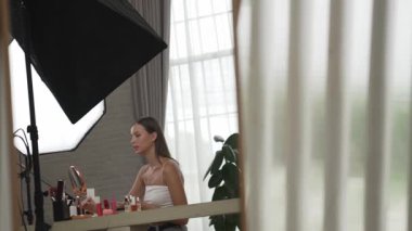 Kozmetik makyajlı genç bir kadın sosyal medya için saç stili video içeriği hazırlıyor. Güzellik blogcusu kameraya gülümserken seyircilere ve takipçilere güzellik bakımını gösteriyor. Düzenle