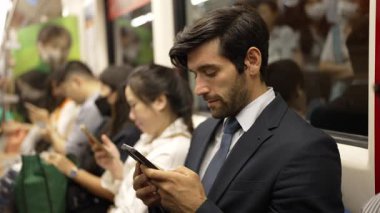 Gülümseyen beyaz iş adamı cep telefonuna bakıyor ya da trende otururken sosyal medya oynuyor. Çekici proje yöneticisi yoğun saatlerde toplu taşıma araçlarını kullanarak iş yerine gidiyor. Sevinçli..