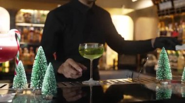 Barmen tarafından sunulan karamelize edilmiş turunçgil dilimli Midori Sour kokteyli, akıllı misafir konuşmacısına kokteyl ve şeker kamışı Noel temalı kokteyl ikram ediliyor. Vinosity.